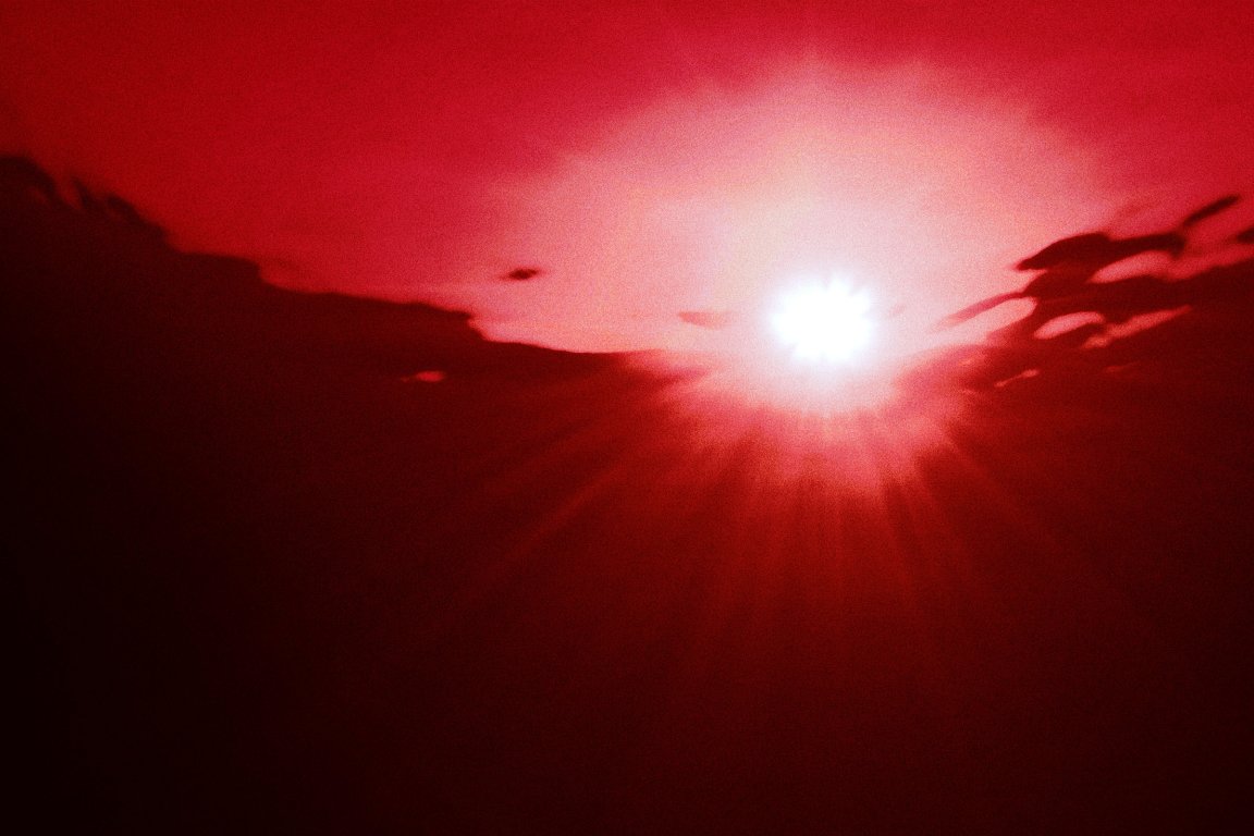 A photograph of the sun from underwater, tinted red.