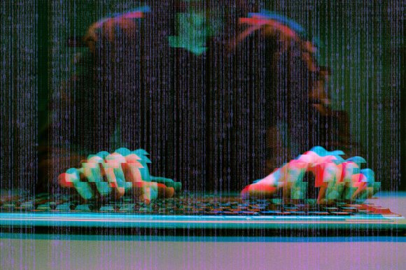 Illustration of an anonymous hacker typing on a keyboard in the dark, overlaid with a digital glitch treatment.
