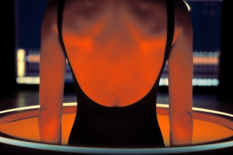 A still from Midjourney's video that shows a woman being lowered into a tube of liquid for scanning.
