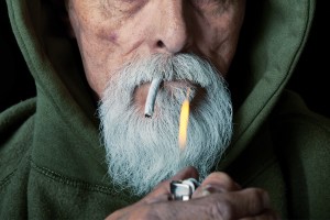 Color-treated photograph of an older man with a marijuana joint in his mouth and a lighter.