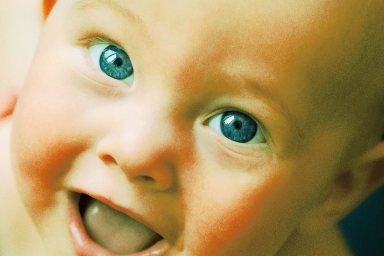 A color-treated photograph of an infant with large eyes staring into the camera and smiling.