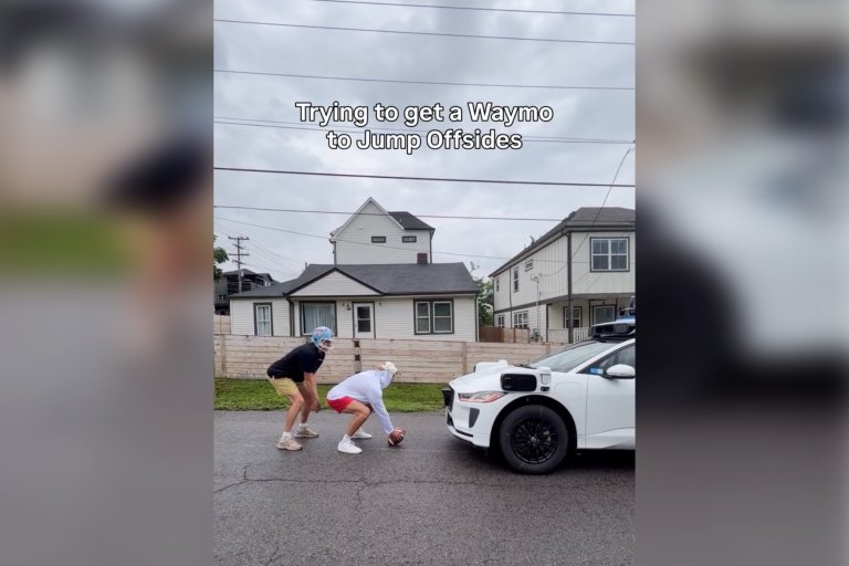 A screenshot featuring two young men in football uniforms attempting to play football with a Waymo.