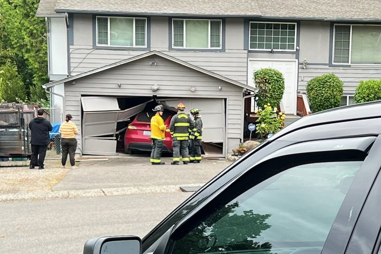 A close-up of a photograph featuring three firemen standing around a Tesla that has crashed through a garage door.