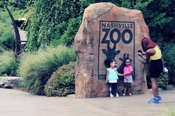 Photograph of a mother taking a photo of her two children in front of the entrance sign for the Nashville Zoo.
