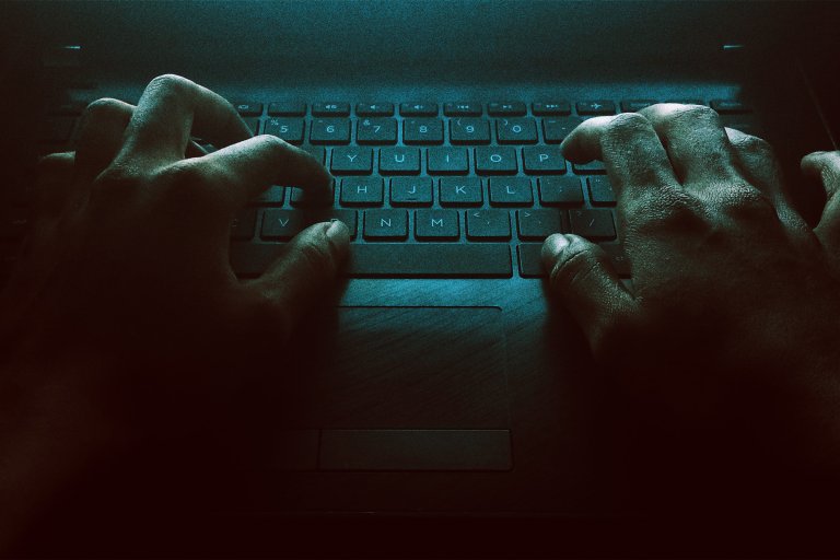 A color-treated photograph of a man's hands operating a keyboard in the dark.
