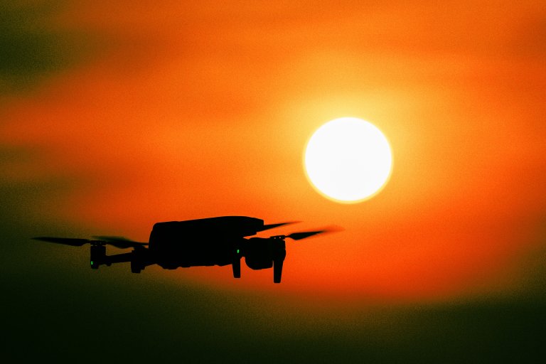 A color-treated photograph of a drone's silhouette in front of the afternoon setting sun.