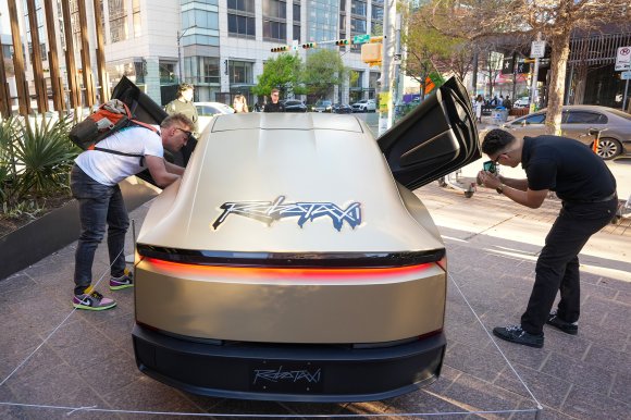Two men look at a Tesla Robotaxi Cybercab on display at a pop-up event at Fareground Austin in downtown Austin during the South by Southwest Conference.