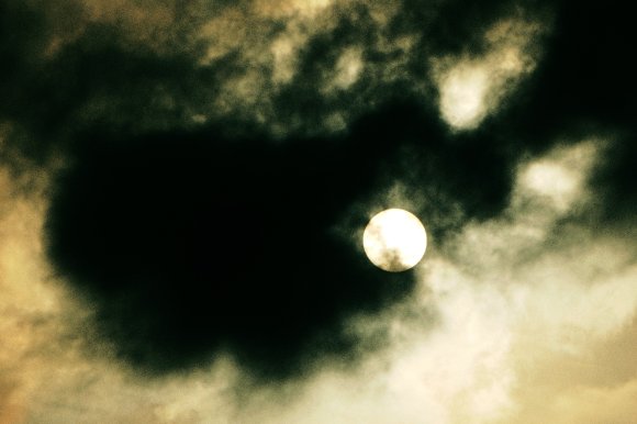 A color-treated photograph of the sun dimmed by smoke and clouds.