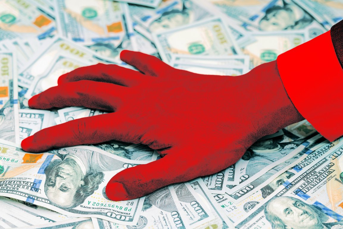 A stylized photo illustration of a businessman's hand grabbing at a pile of money.