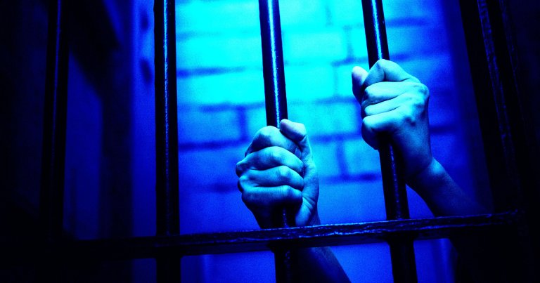 A color-treated photo of two hands grasping jail cell bars.