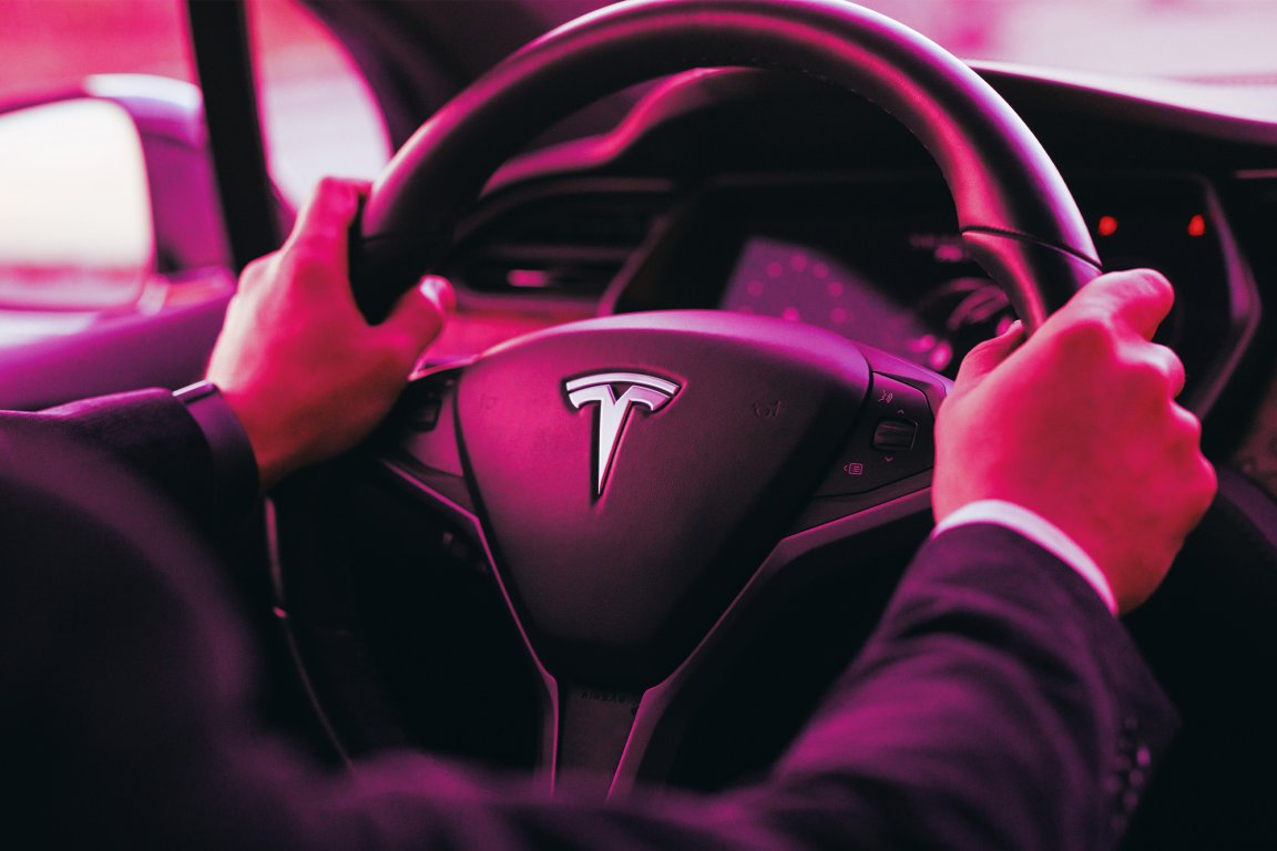 A color-treated photograph of a driver with their hands on a Tesla steering wheel.