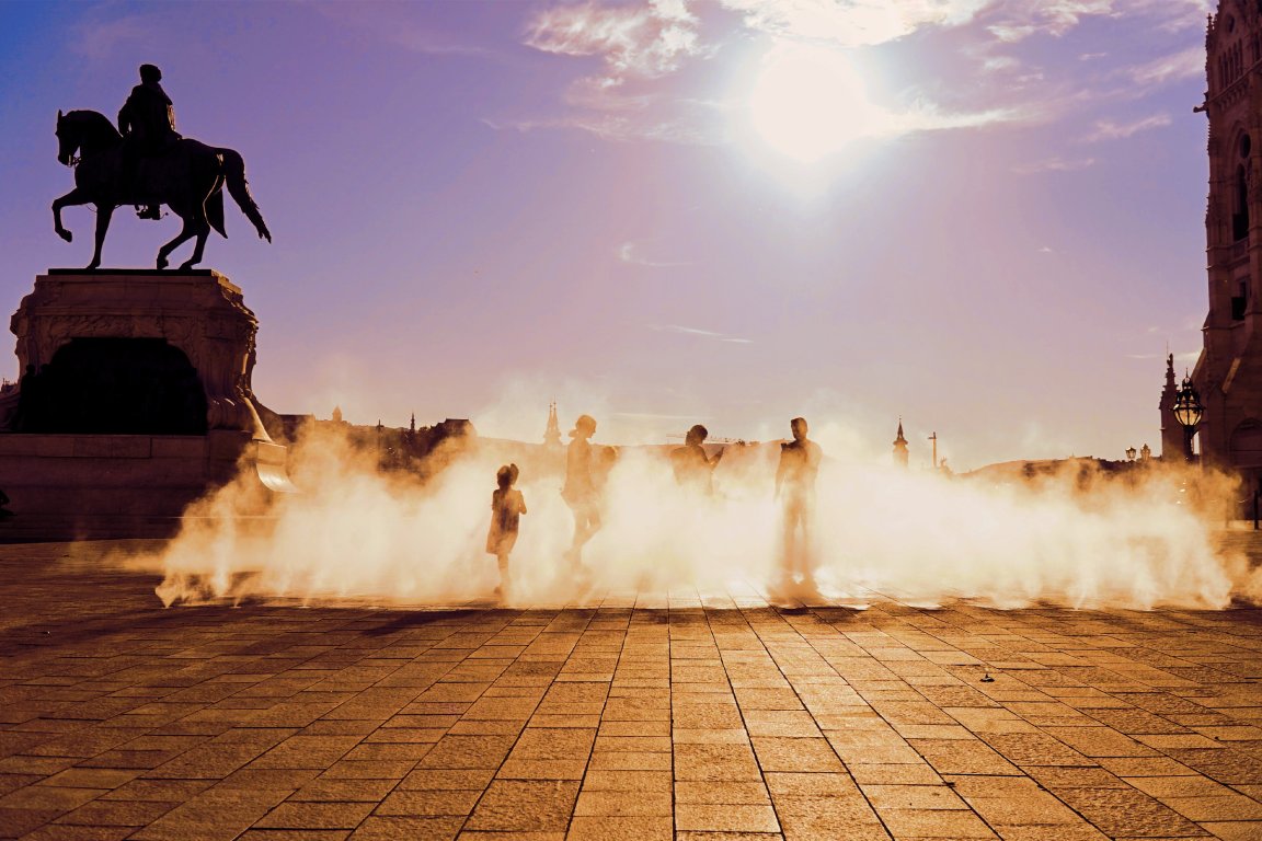 A color-treated photograph of people enjoying the coolness of the water sprayers in the summer heat at Kossuth square in Budapest, Hungary.