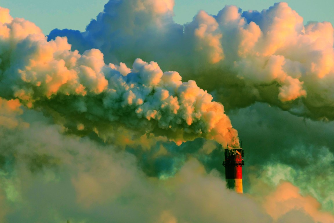 A color-treated photograph of a smoke stack surrounded by clouds of thick acrid smoke.