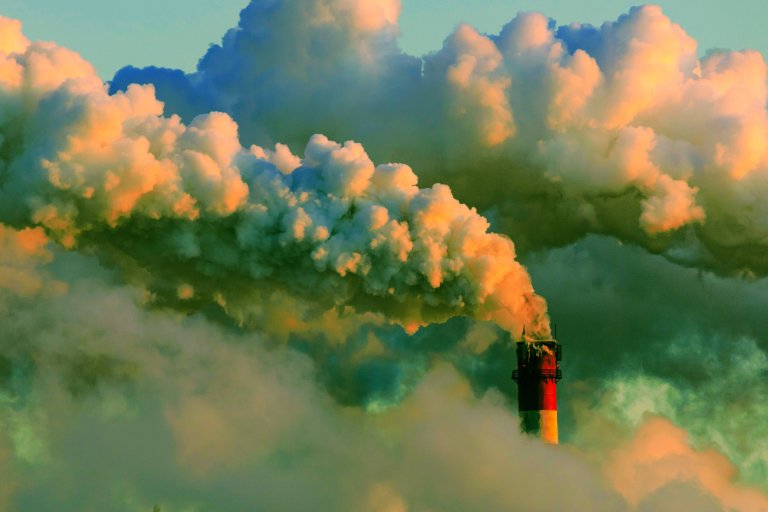A color-treated photograph of a smoke stack surrounded by clouds of thick acrid smoke.