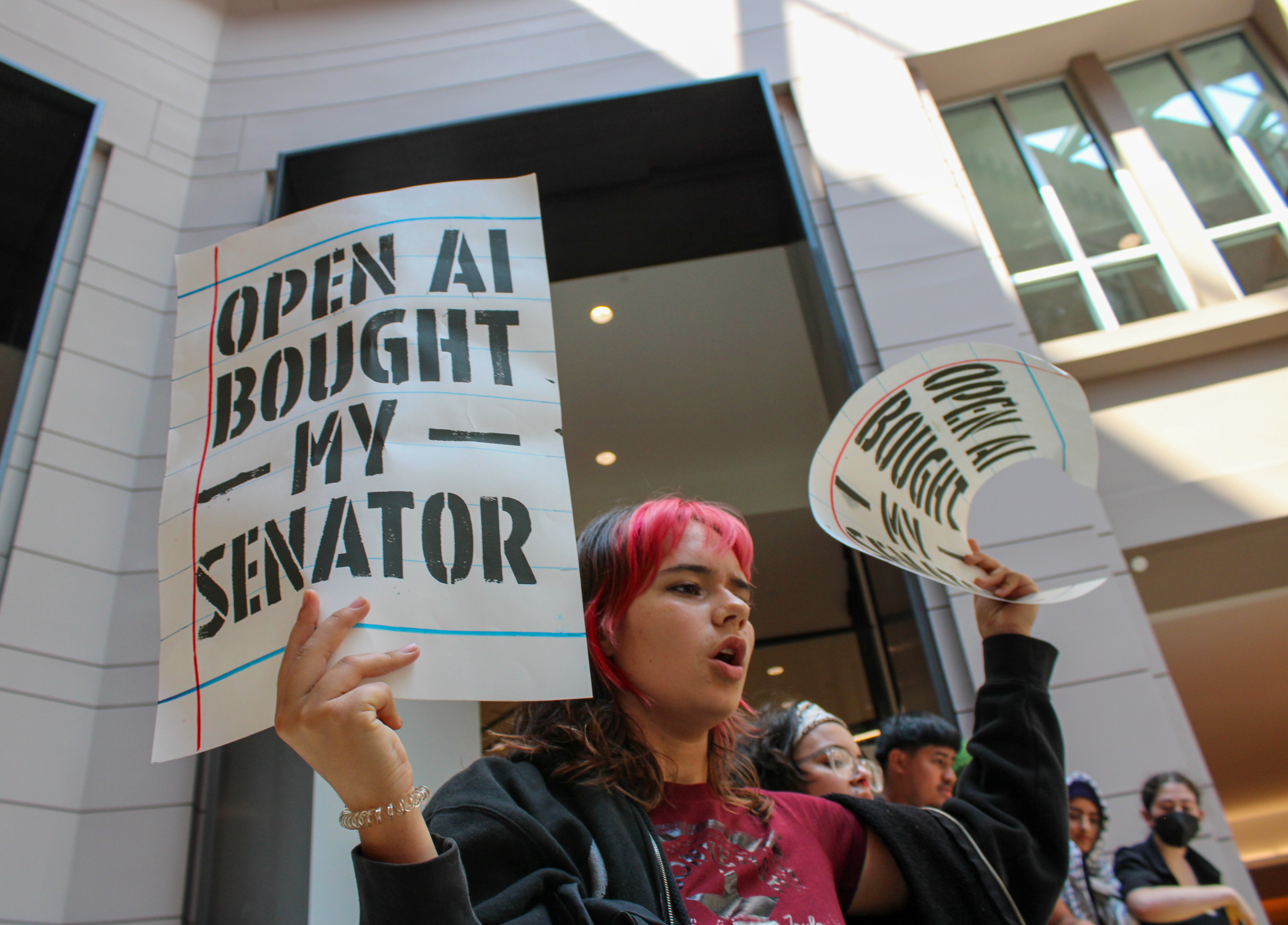 A protester holds a sign that says "OpenAI bought my senator"