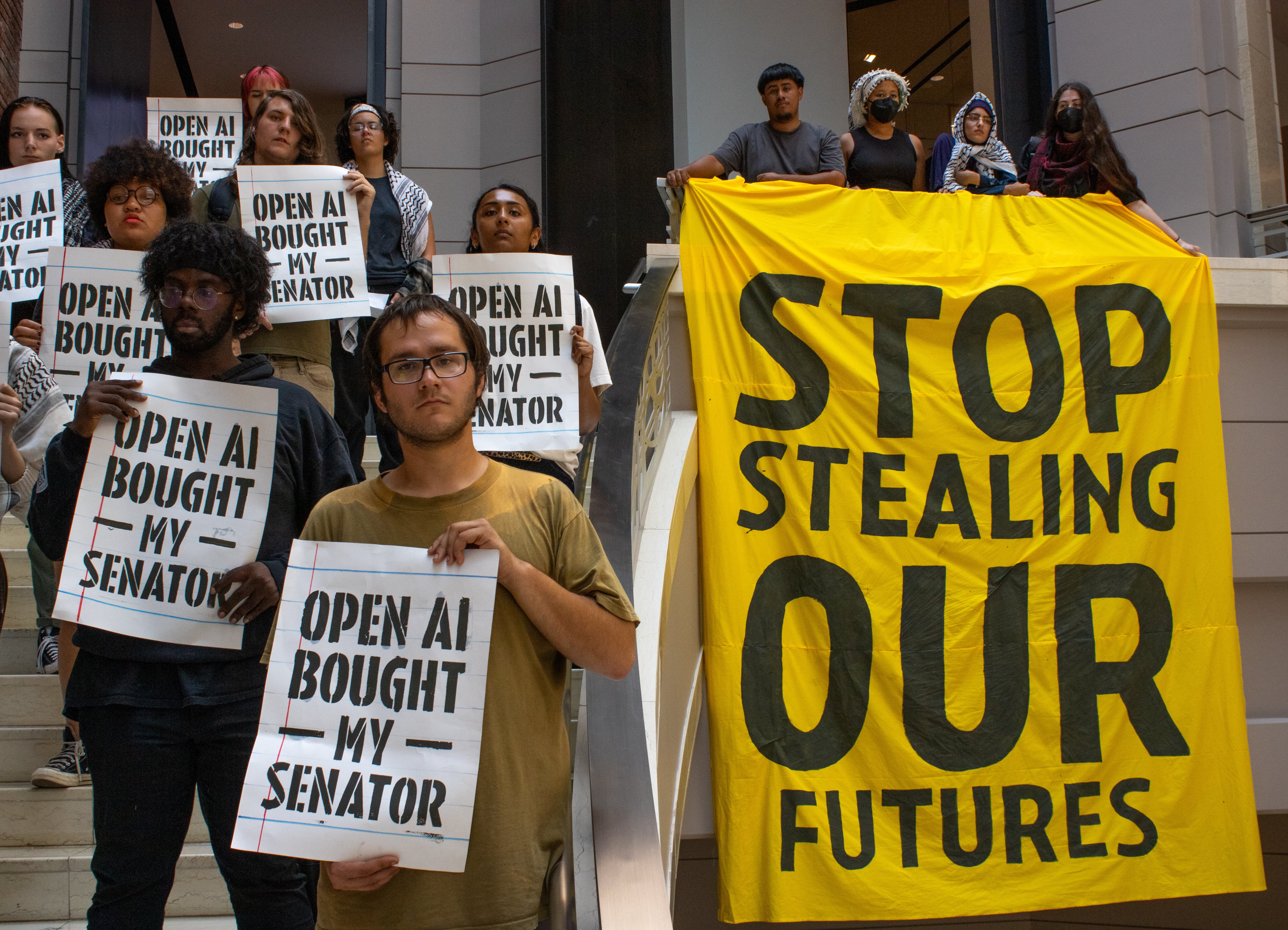 A group of protesters are holding signs that say "OpenAI bought my senator" and unfurling a banner that says "stop stealing our futures"