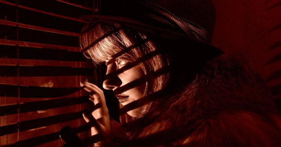 A picture of a woman in a wig staring through blinds.