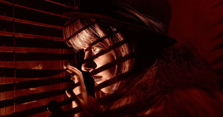 A picture of a woman in a wig staring through blinds.