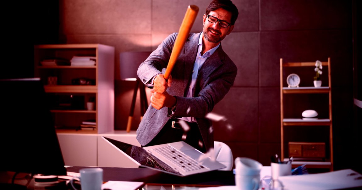 A photo of a man using a baseball bat to smash a laptop.