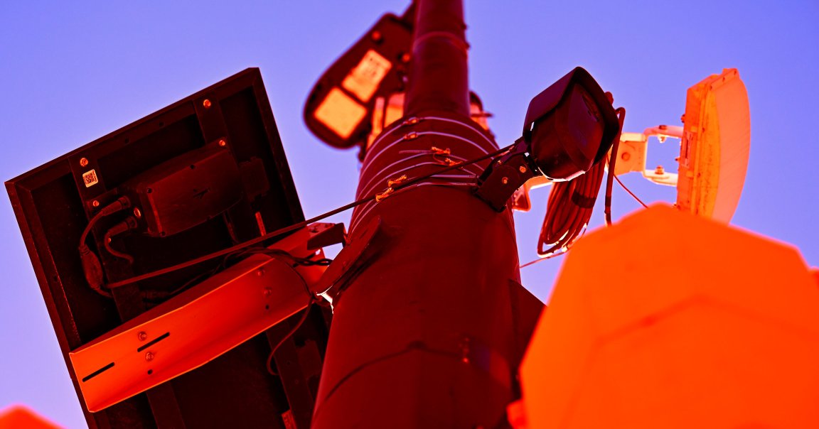 A Flock Safety license plate recognition camera is seen above a traffic signal on a post.
