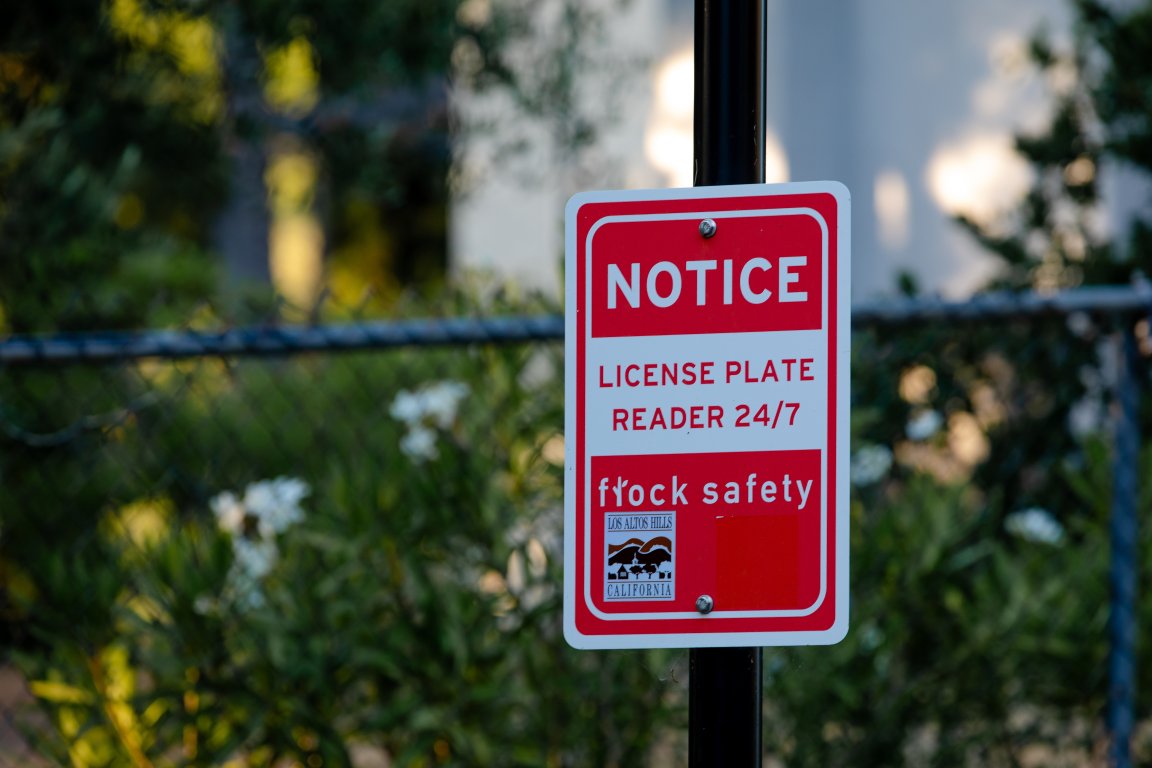 Red and white sign informing drivers that Flock cameras are collecting license plates.