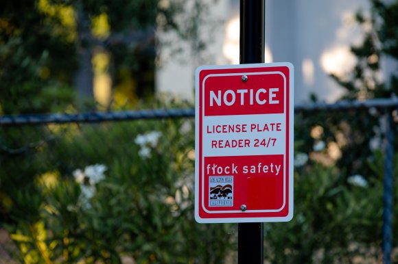 Red and white sign informing drivers that Flock cameras are collecting license plates.