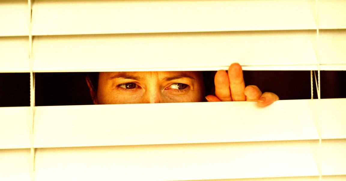 A photo of a woman staring through closed blinds.