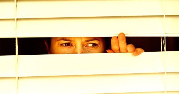 A photo of a woman staring through closed blinds.