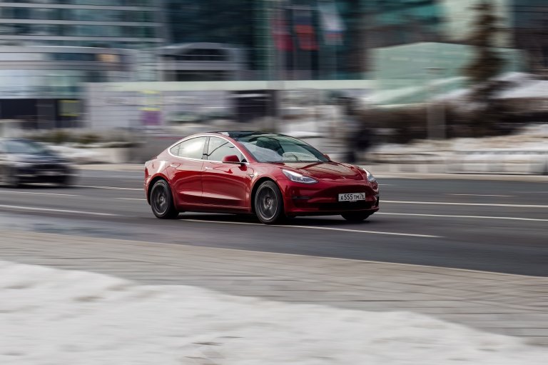 A red Tesla is shown driving down a street.
