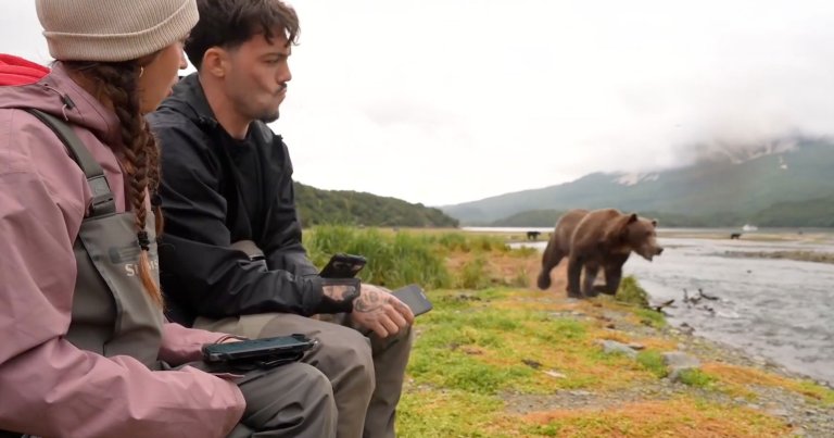 A screenshot of two streamers sitting near a grizzly bear hunting for fish.