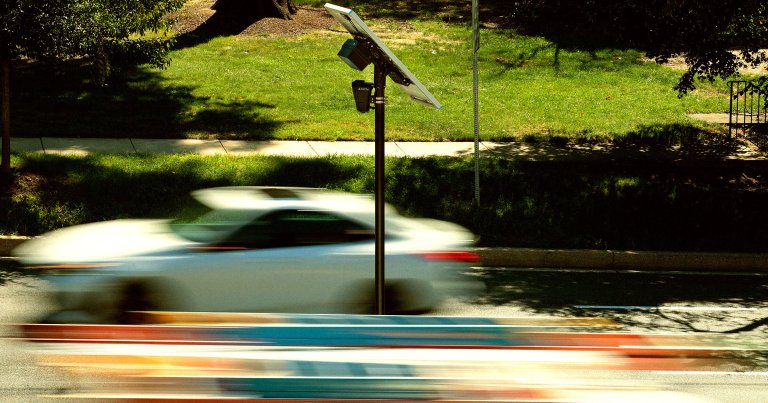 Traffic flows past an Axon brand automatic license plate reader (ALPR) camera.
