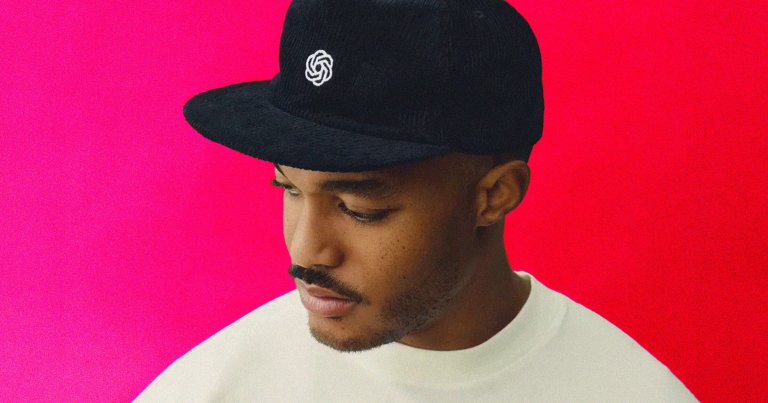 A photo of a model wearing a hat with the OpenAI logo on it.