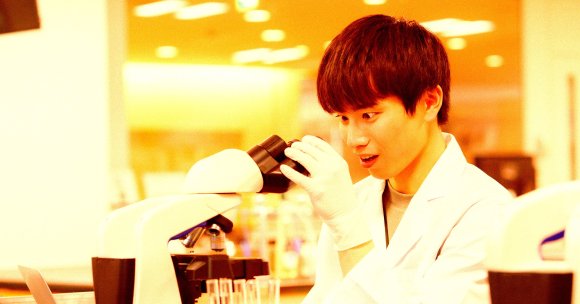 A color-treated photo of a student staring into a microscope in a lab.