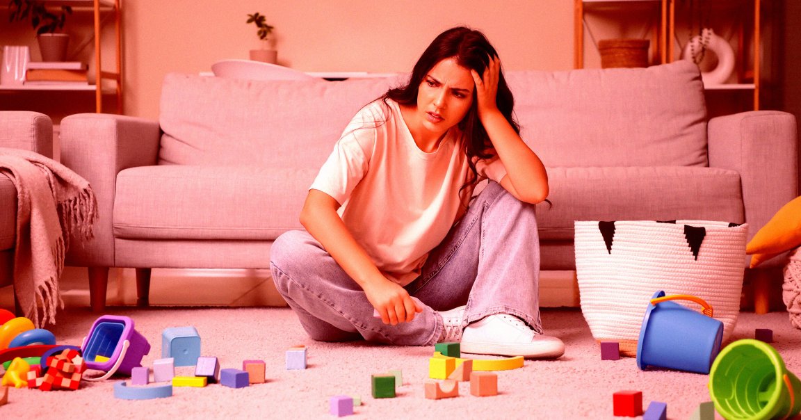 Tired young mother resting among scattered children's toys at home.