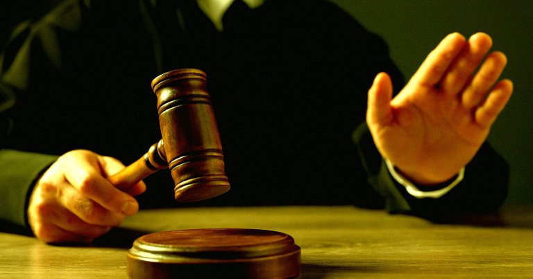 A judge raising his hands while holding a gavel.