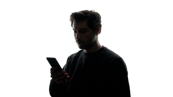 A photo illustration shows the silhouette of a man using a phone against a white background.