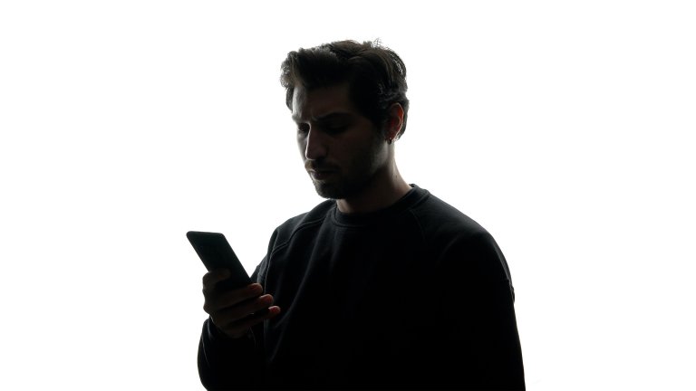 A photo illustration shows the silhouette of a man using a phone against a white background.
