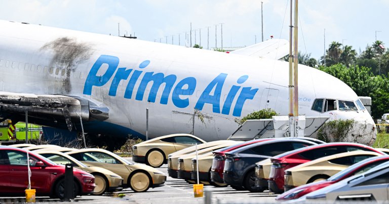A parking lot filled with Tesla Cybercabs is seen in the foreground as the nose of a Prime Air cargo plane rests on the ground after the aircraft overran the runway and struck cars the previous day at Miami International Airport in Miami, Florida, on September 7, 2026.