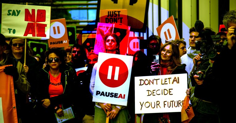 A group of protesters holding signs with messages opposing AI, including "SAY NO TO AI," "PAUSE AI," and "DON'T LET AI DECIDE YOUR FUTURE." Some signs feature a red pause symbol. The crowd includes people wearing sunglasses and holding cameras, indicating media coverage. The setting appears to be outdoors in an urban area.