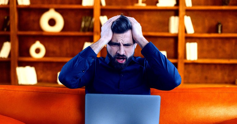 A man holding his had while looking at a laptop.