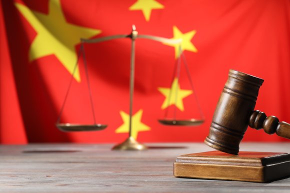 A gavel and legal scales set before a Chinese flag.