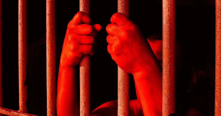 A color-treated photo of a pair of hands holding onto prison cell bars.