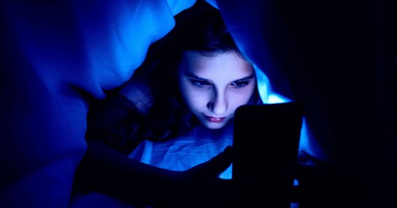 A girl looking at a smartphone screen under a blanket.