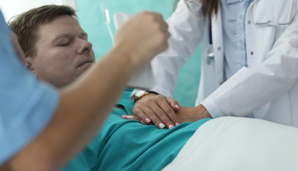 A patient is shown lying in a hospital bed as a medical professional performs chest compressions.