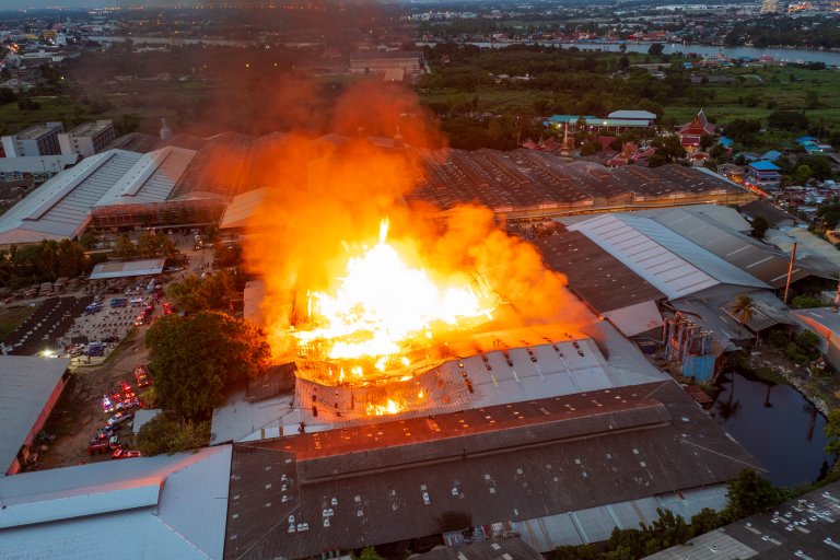 A photo shows a large building engulfed in intense flames and thick smoke during a fire.