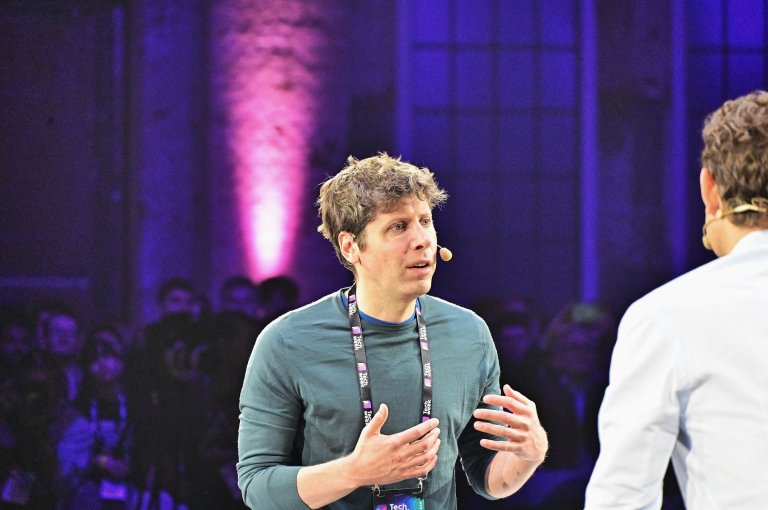 OpenAI CEO Sam Altman is shown with a headset microphone at an event.