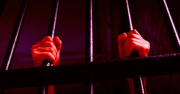 A person's hands holding onto jail cell bars.