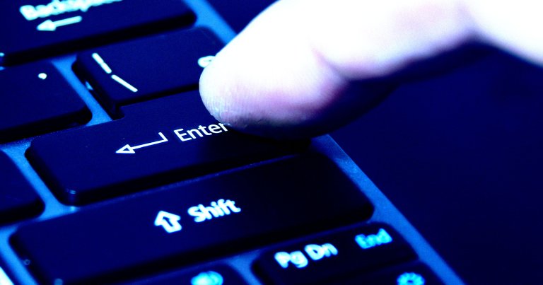 A finger hitting the Enter button on a keyboard.