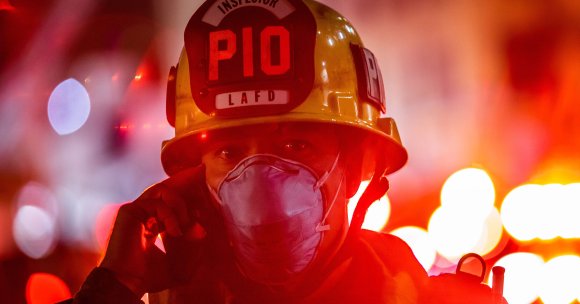 A Los Angeles Fire Department Public Information Officer wearing a facemask speaks on the phone.