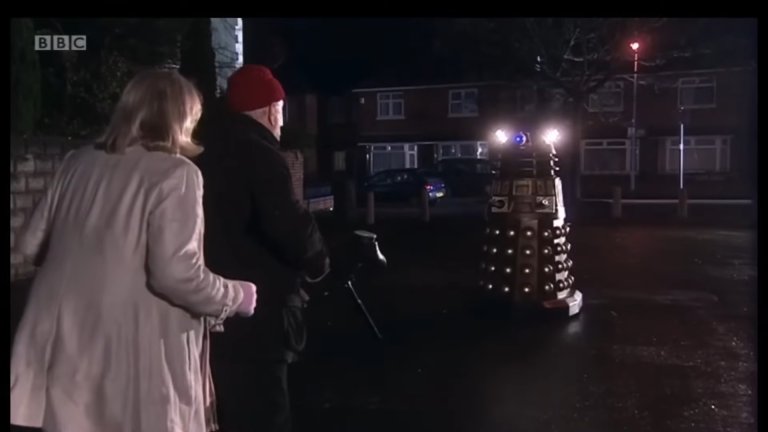 A screenshot from "Doctor Who" shows a Dalek villain in a neighborhood setting.